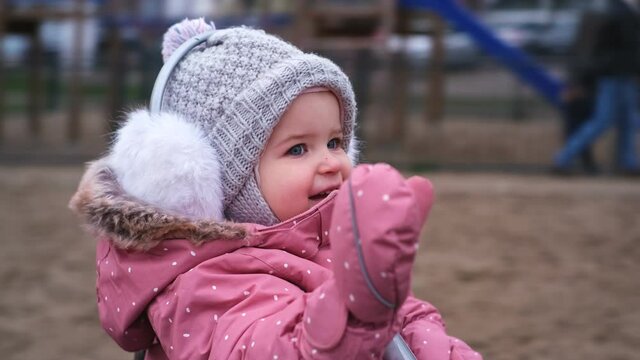 Young Happy Caucasian Toddler Girl in Warm Clothes Having Fun On Public Playground Carousel on Cold Autumn Winter Day