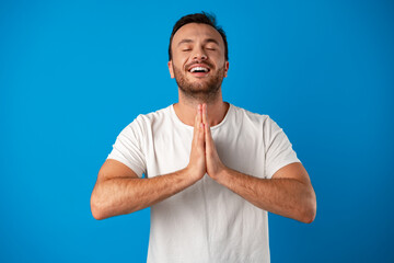 Focused handsome young man meditating on camera over blue background