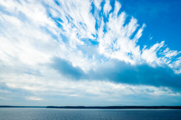 River landscape. Calm water and beautiful blue sky with clouds. Trees grow on the nearest shore. There is copy space.