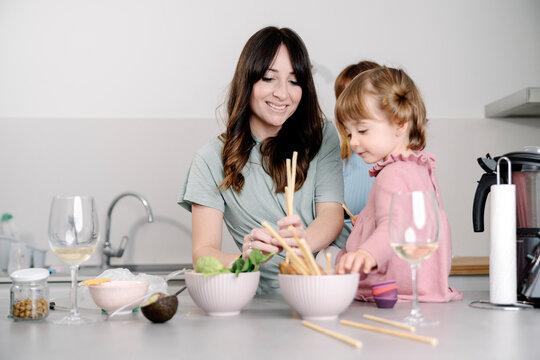 Mum putting breadsticks while her daughter eats 