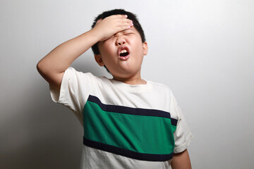 Frustrated Little Asian boy screaming with a hand holding his head isolated on grey background.
