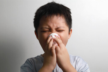 Cropped shot of an adorable little boy blowing his nose while standing against a white wall.