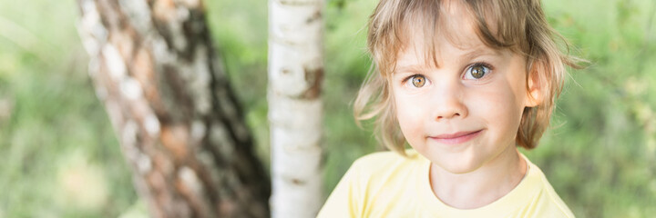 motion blur defocused photo of portrait smiling sunny kid caucasian candid boy with blonde long wavy or curly hair and sunlight on face on nature countryside forest outdoor. banner