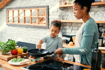 Black little girl and her mother prepare food together in kitchen.