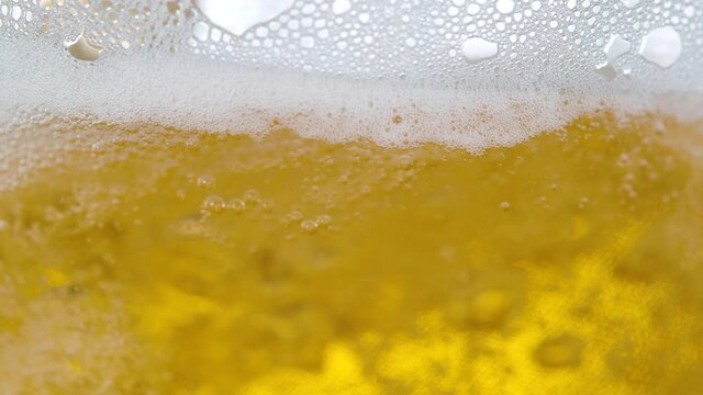 SLOW MOTION, MACRO, DOF: Refreshing crips golden pale ale gets poured into a large jug. Bubbling beer splashing around the glass as it gets poured from a pub tap. White bubbles rising to the top.
