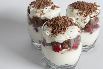 Biscuit cake with cream and cherries in a glass on a white background