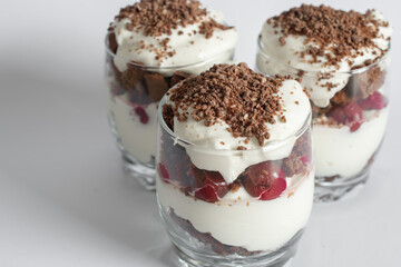 Biscuit cake with cream and cherries in a glass on a white background