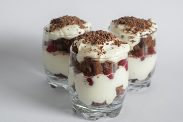 Biscuit cake with cream and cherries in a glass on a white background