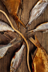 Tails of salted dried and smoked fish of different sizes on wooden surface with rope