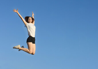 Fototapeta na wymiar Positive sport girl on background of blue sky. Slender woman jumping. Keep fit