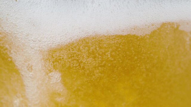 SLOW MOTION, MACRO, DOF: Bubbling beer splashing around the glass as it gets poured from a pub tap. Refreshing crips golden pale ale gets poured into a large jug. White bubbles rising to the top.