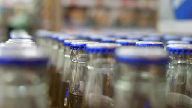 Close up of bottles row with blue caps in a big supermarket with a man walking on the background