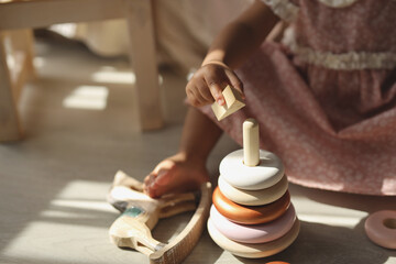 a dark-skinned girl is sitting on the floor of the house and playing with a wooden pyramid. the concept of environmental friendliness and children's goods. high-quality photography