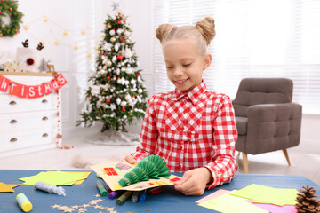 Cute little child with beautiful Christmas card at table in decorated room