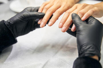 Master manicurist in black gloves is holding thin and neat fingers