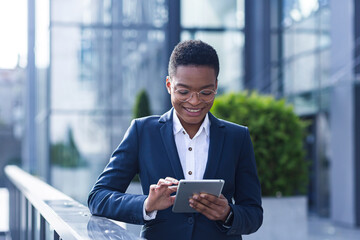 Successful business woman smiling and happy enjoys tablet computer during break, african american woman at office outside