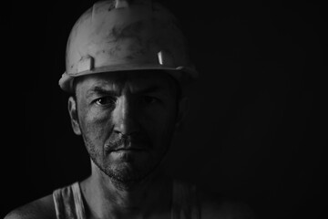Portrait miner in helmet and undershirt with dirty face.