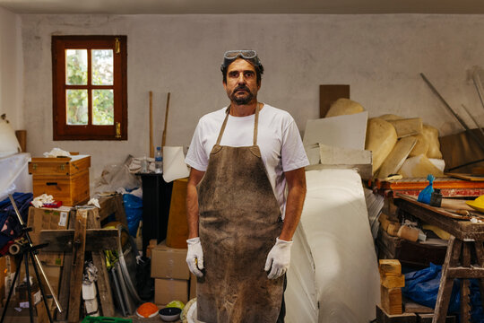 Portrait of artisan in apron in messy workshop