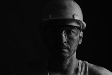 Portrait of a miner wearing a helmet, goggles and a undershirt with a dirty face.