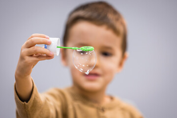 Happy little kid blowing soap bubble at home. Child indoor activity concept. Little caucasian boy...