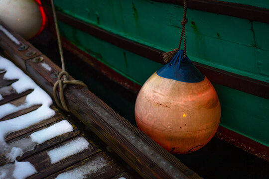 Orange buoy on a green boat next to a snowy dock