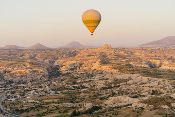 Cappadocia, Turkey - 21 July 2021: Colorful hot air balloon flying over white mountains in sunrise sky. Goreme mountains scenic view