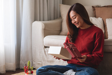 Portrait image of a young woman receiving and opening a red present box at home