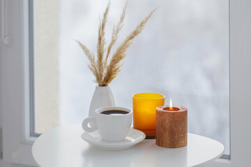 cup of coffee with burning candles  on white table by window on winter