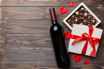 Bottle of red wine on colored background for Valentine Day with gift and chocolate. Heart shaped with gift box of chocolates top view with copy space
