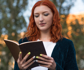 A young and attractive redhead Caucasian girl is reading a book. Education concept.