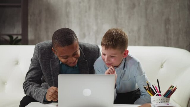 Positive boy pupil watches funny video via laptop and laughs understanding meaning with native speaker English teacher help at home private tuition slow motion