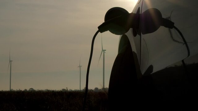 Electric car charged by windmills on cloudy day. Powerful wind machines rotate in field producing clean energy at rural substation close view