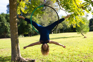 Blonde woman and young gymnast acrobat athlete performing aerial exercise on air ring outdoors in park. Lithe woman in blue costume performs poses of circus performers dancing with hips