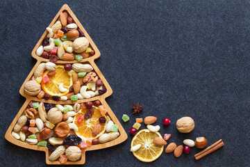 Christmas mix of dried fruit and nuts in christmas tree-shaped bowl on dark background