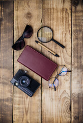 Sunglasses, camera, notepad and magnifying glass on a wooden background. Summer time, vacation, travel, tourism.