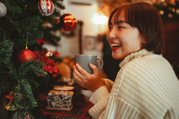 Happy women holds a cup of coffee and smell aromatic near a Christmas tree decoration