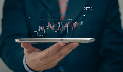 Businessman holding tablet 2022 stock market forecast outlook, charts and candlesticks, stock...