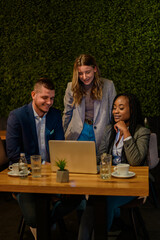 Cheerful work colleagues working on a laptop while having a meeting in a cafe