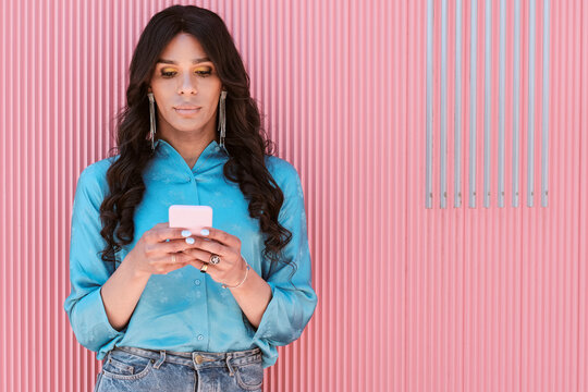 Fashionable non-binary woman using mobile phone in front of corrugated pink wall