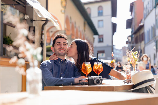 Young woman kissing man at sidewalk cafe during sunny day