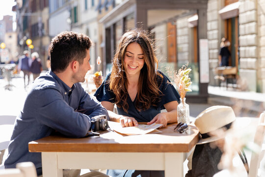 Tourists checking map while sitting at sidewalk cafe in city