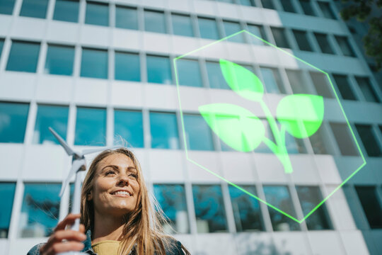 Smiling woman with windmill model looking at plant logo near building