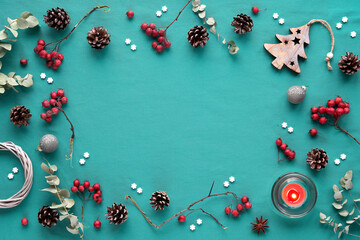 Fototapeta premium Natural low impact Xmas decor. Christmas background in turqiouse and red, copy-space. Flat lay, hawthorn berry, eucalyptus, wattle wreath, Xmas tree toy, balls, candle, pine cones, sugar snowflakes.