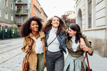 Smiling friends walking with arm around on each other in city