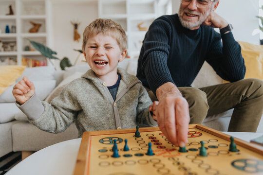 Cheerful son playing ludo game with father at home