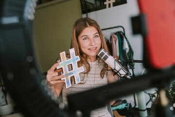 Girl holding hashtag symbol while vlogging at home