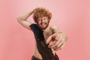 Cropped portrait of cheerful man in character of neanderthal joyfully pointing at camera, posing...