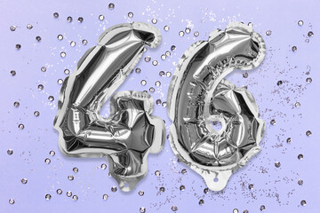 Silver foil balloon number, digit forty six on a lilac background with sequins. Birthday greeting card with inscription 46. Anniversary concept. Top view. Numerical digit. Celebration event, template.