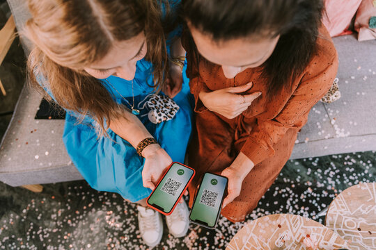 Women holding smart phones with barcode on screen while sitting at home