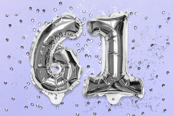 Silver foil balloon number, digit sixty one on a lilac background with sequins. Birthday greeting card with inscription 61. Top view. Numerical digit. Celebration event, template.